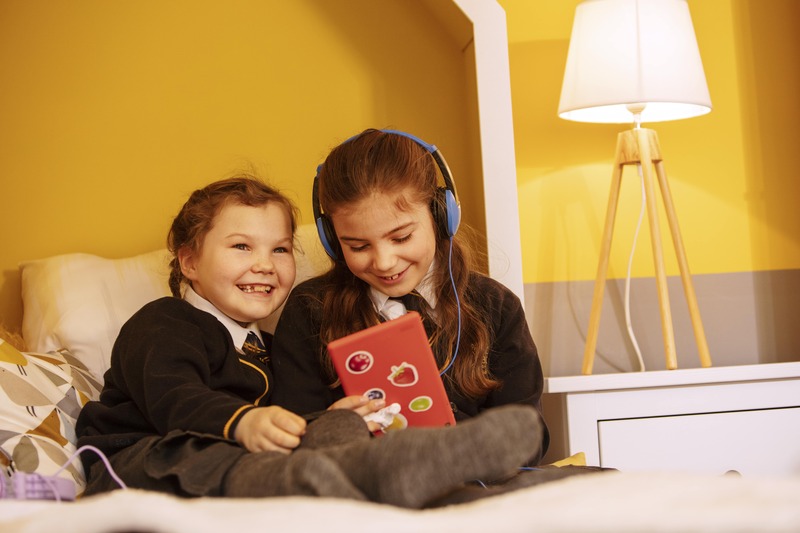 Two children sitting on bed playing with ipad