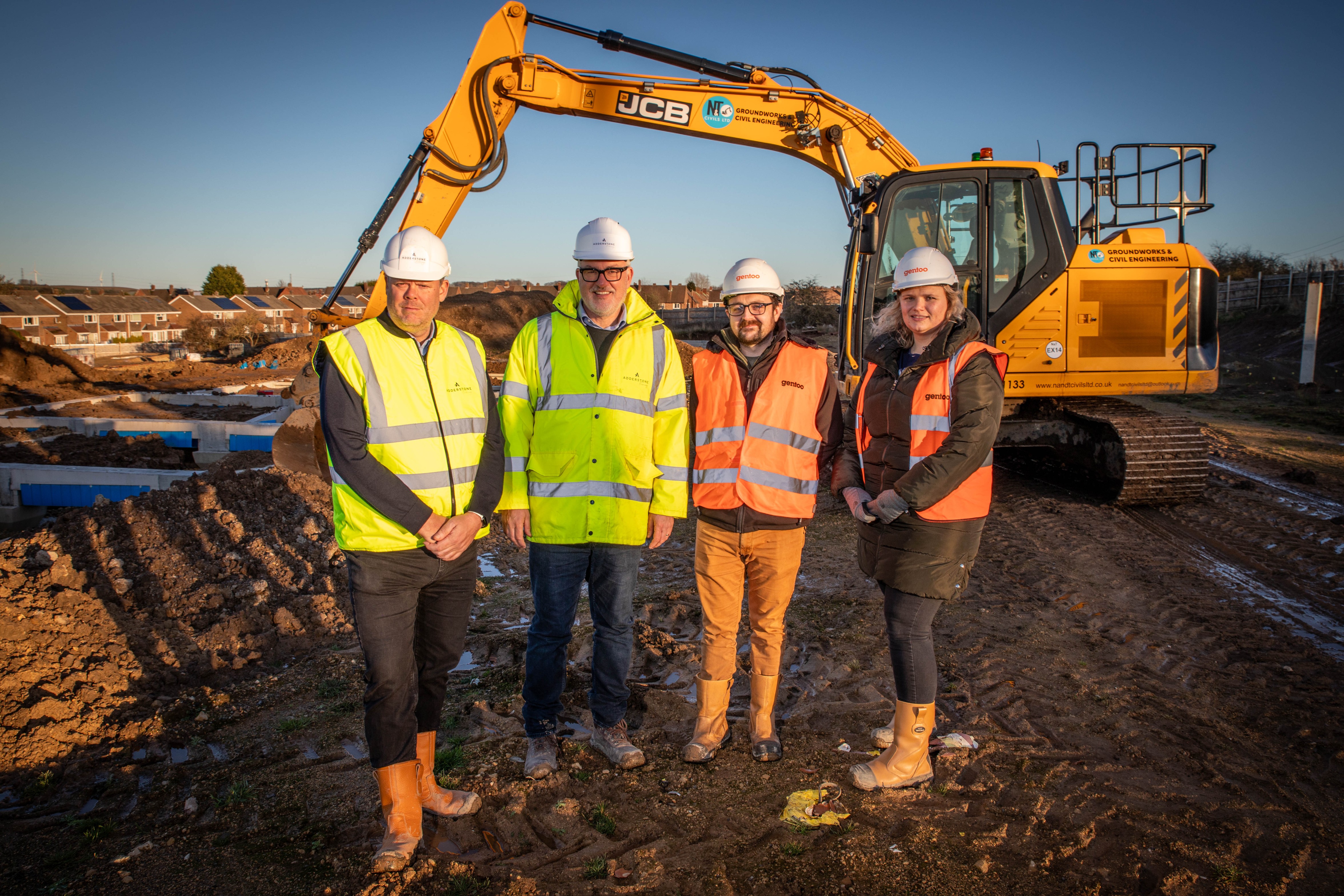 Four people stood on a building site with digger in background