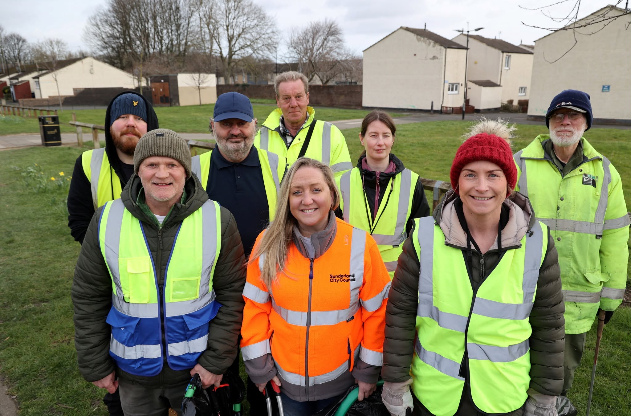 Group of community volunteers wearing high-visibility jackets standing together in a residential green space.